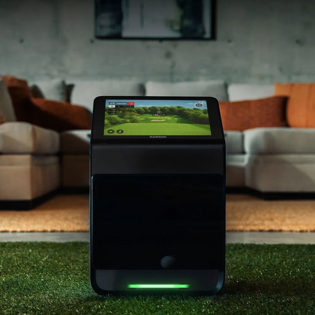 A modern golf launch monitor set up on a driving range turf mat behind a golf ball.