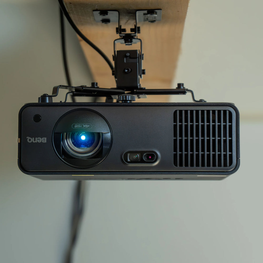 BenQ AK700ST 4K Laser Golf Simulator Projector mounted to a wooden beam, with its lens glowing blue