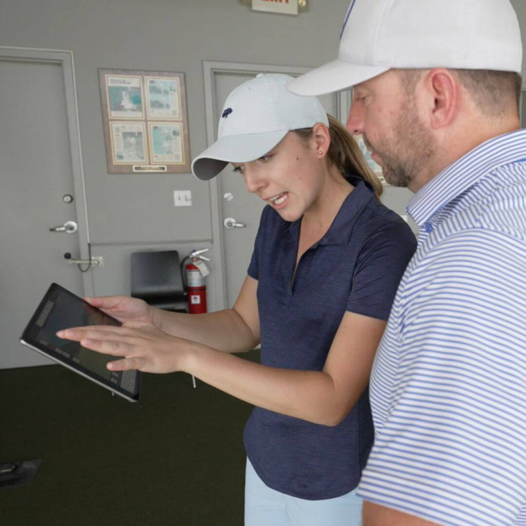 two golfers looking at ipad with golf simulation data shown.